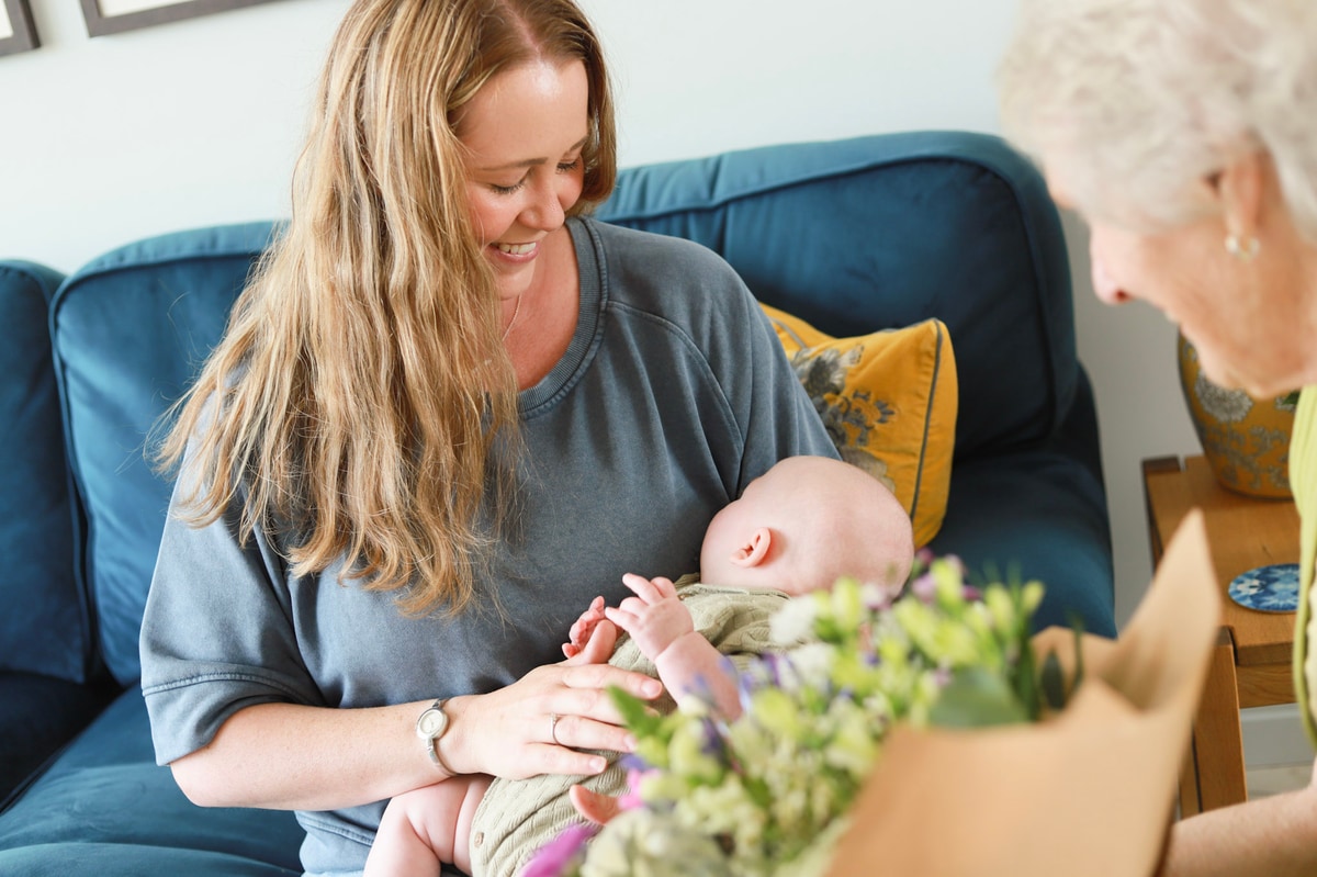 Mother holding baby with same day bouquet from local florist in foreground